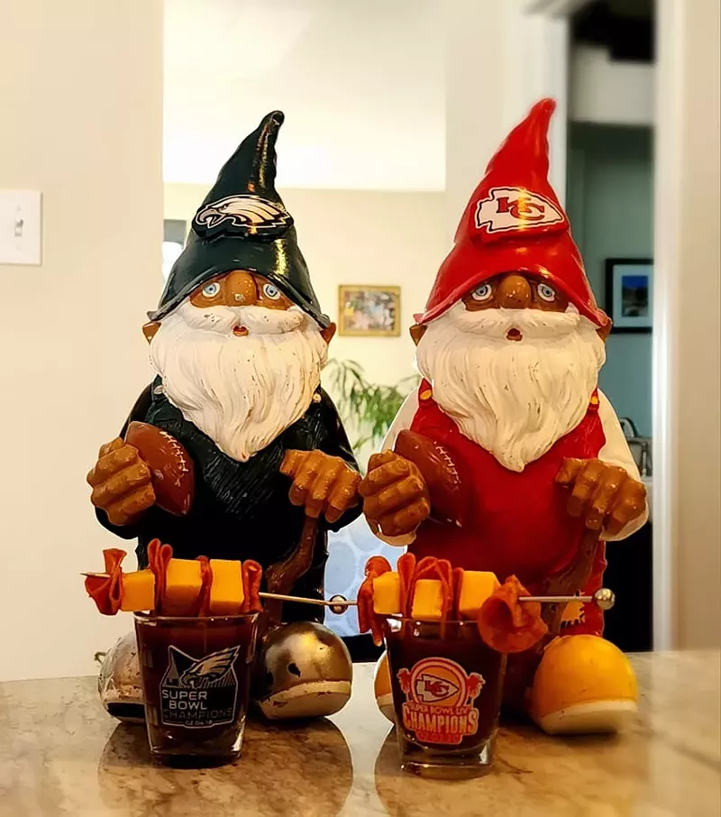 An Eagles and Chiefs gnome stand side to side in front of shot glasses for their respective teams.