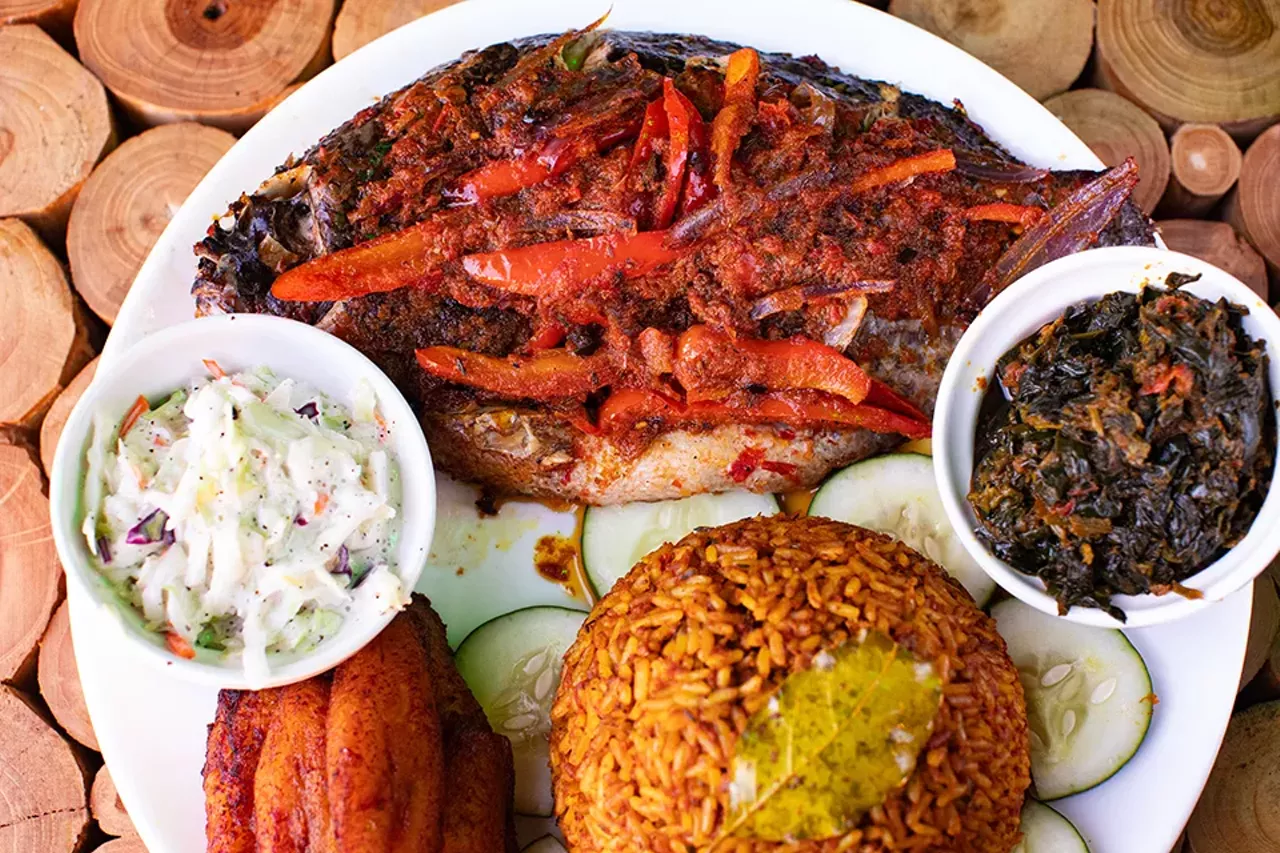 Tilapia plate with grilled whole tilapia fish marinated in stew sauce with sautéed bell peppers and onions, served with a side of cole slaw or sautéed veggies, jollof rice and plantains.